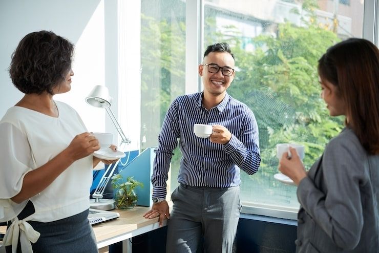 Tre kollegor tar en fikapaus med kaffe i ett ljust kontor